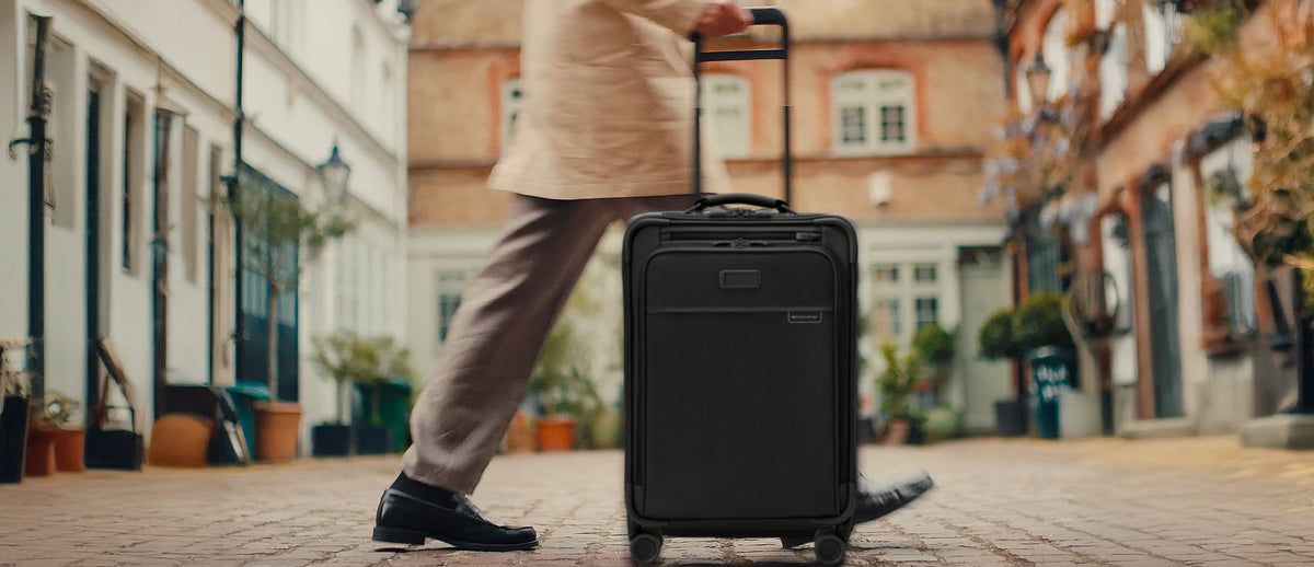 Person pulling a black suitcase on a street with buildings in the background