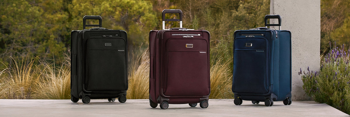 Three suitcases in black, maroon, and blue on a wooden surface with a natural background.